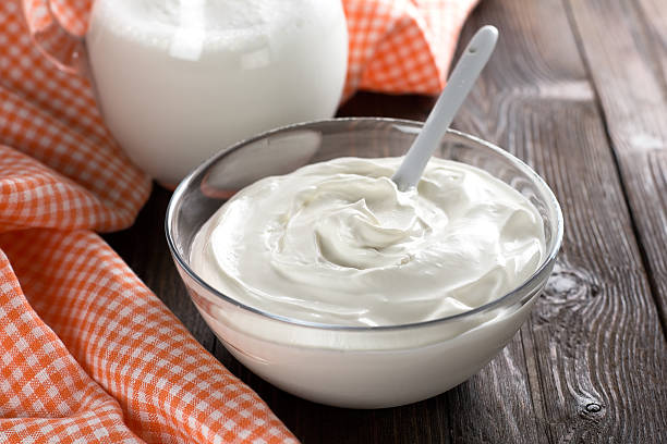 Glass bowl full of sour cream beside cloth on a wooden table stock photo