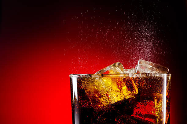 Glass cup of iced cola on red background Ice cola with splashing CO2 bubbles cola stock pictures, royalty-free photos & images