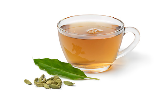 Glass cup with Cardamom tea and a heap with cardamom seeds and leaf in front isolated on white background