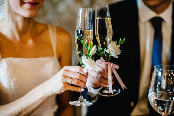 Glass decorated with flowers and greenery on the background newlyweds. close up. The bride and groom hold glasses of champagne in their hands. Wedding ceremony. stock photo