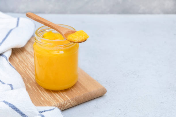 Glass jar of clarified butter (ghee) with wooden spoon on neutral concrete background. Image with copy space Glass jar of clarified butter (ghee) with wooden spoon on neutral concrete background. Image with copy space ghee stock pictures, royalty-free photos & images