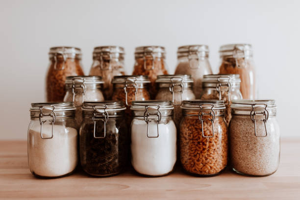 Glass jars full with dried uncooked food ingredients. Organized food containers on wooden table in front of a white background. 
Different type of dried, uncooked ingredients in air tight containers. pantry stock pictures, royalty-free photos & images