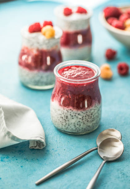 glass jars with chia pudding with raspberry and jam. Bowl of raspberry berry on the blue background. stock photo