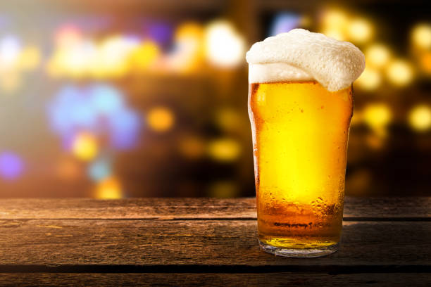 glass of beer on a table in a bar on blurred bokeh background glass of beer on a table in a bar on blurred bokeh background pint glass stock pictures, royalty-free photos & images