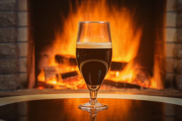 A glass of Beer with foam near cozy fireplace burning background. stock photo