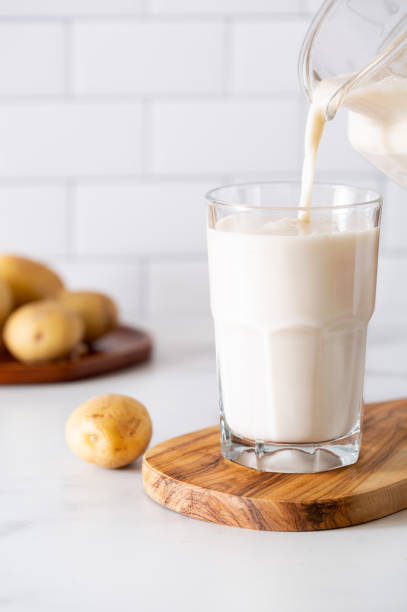 Glass of homemade potato milk with raw potatoes; copy space stock photo