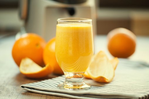 Glass of real freshly squeezed orange juice. Ambient light with juicer and oranges in background.