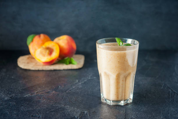 Glass of peach fruit smoothie with mint leaves and ingridients on the dark background. Healthy, vegetarian, vegan diet food. Selective focus, space for text. Glass of peach fruit smoothie with mint leaves and ingridients on the dark background. Healthy, vegetarian, vegan diet food. Selective focus, space for text peach smoothie stock pictures, royalty-free photos & images