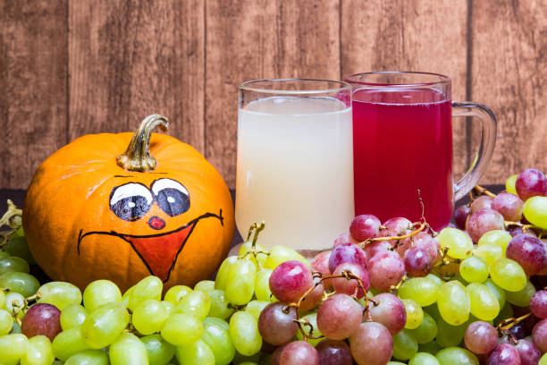 glass of red stum and 2 glasses of white stum together with some green and red grapes and a pumpkin photographed in front of a piece of wood. - sturm imagens e fotografias de stock