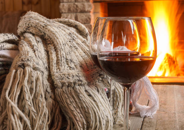Glass of red wine  and wool  things near cozy fireplace. stock photo