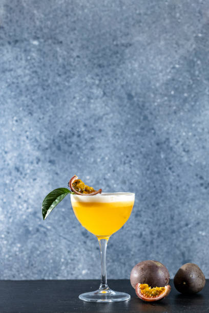 Glass of refreshing passionfruit Martini cocktail served on gray table surface surround of fresh passion fruit, shallow depth of the field. stock photo