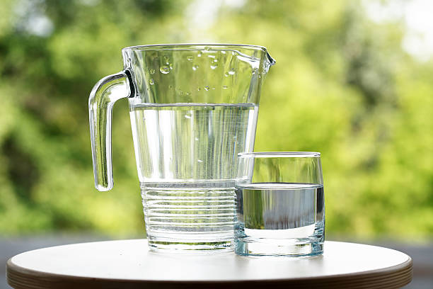 Glass Of Water Glass of water near jug on green nature background jug stock pictures, royalty-free photos & images