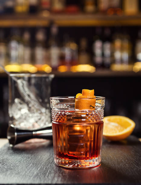 Glass of  whiskey (cognac or brandy) with lemon and ice cubes standing on the bar counter with a bottle on the background stock photo