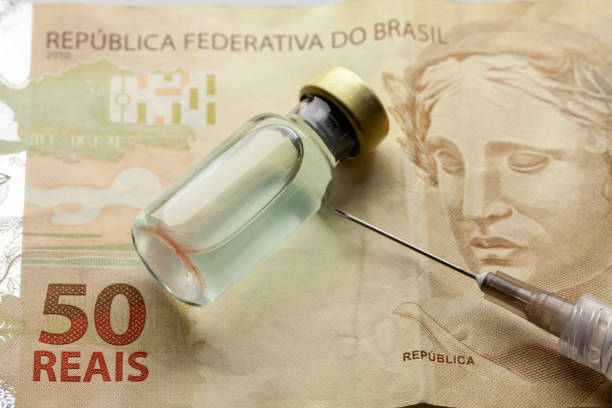 Glass vaccine bottle with liquid and syringe needle over a brazilian "50 Reais" bank note from close stock photo