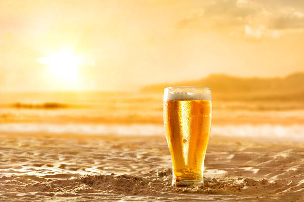 Glass with fresh beer on the sand golden sunset background stock photo