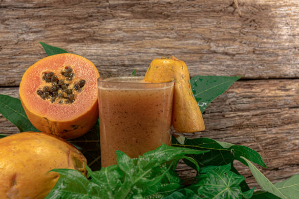Glass with papaya juice. Tropical fruit Glass with papaya juice. Tropical fruit. Edible fruit with digestive properties. Green leaves. Wood background. Fruit for juices. Natural food and detox. Fresh papaya fruit. papaya smoothie stock pictures, royalty-free photos & images