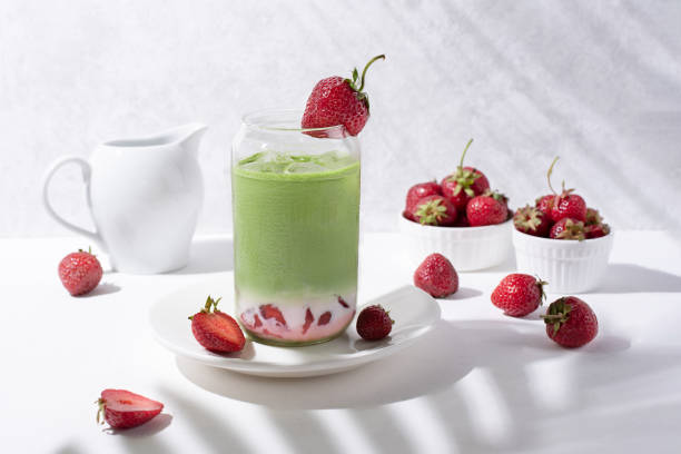 Glass with strawberry matcha latte with strawberries on a white background with beautiful shadows from the branches. Glass with strawberry matcha latte with strawberries on a white background with beautiful shadows from the branches, close-up. Strawberry Matcha Milk stock pictures, royalty-free photos & images