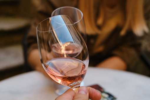 A glasses of rose wine in the hands of a girl and man who relaxing on restaurant terrace. Summer holiday. Celebrate and enjoy moment. Alcoholic drink tasting. Romantic evening aperitif. Wine glass closeup