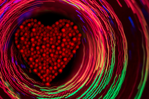 Glittering red heart inside the glowing multi colored circles on a dark background.