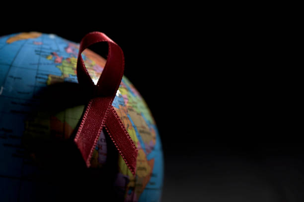 globe with a red ribbon for the fight against AIDS closeup a world globe with a red ribbon for the fight against AIDS on a black background with a blank space on the right world aids day stock pictures, royalty-free photos & images