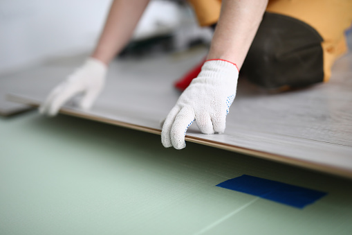 Gloved technician lays down laminate on backing. Construction flooring services concept