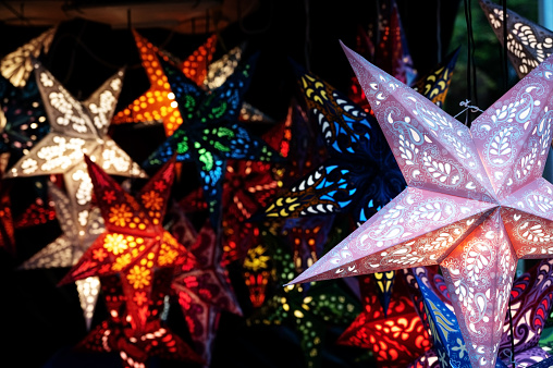 Glowing Christmas lanterns in star shape from folded paper in a market booth at night, selling light for the dark winter holidays, copy space, selected focus narrow depth of field