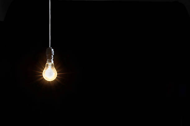 Glowing lightbulb against black background stock photo