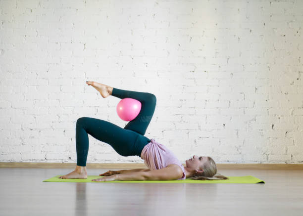 Gluteal bridge with pink small fit ball. Caucasian girl doing pilates with special equipment in fitness studio. Gluteal bridge with pink small fit ball. Caucasian girl doing pilates with special equipment in fitness studio. Work out, yoga, balance, concentration, healthy spine, sport, smart body and wellness concept yoga ball work stock pictures, royalty-free photos & images