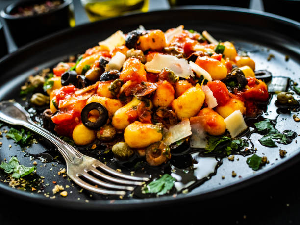 Gnocchi puttanesca - gnocchi with tomato sauce, anchovies, chili, capers and olives on wooden black table stock photo
