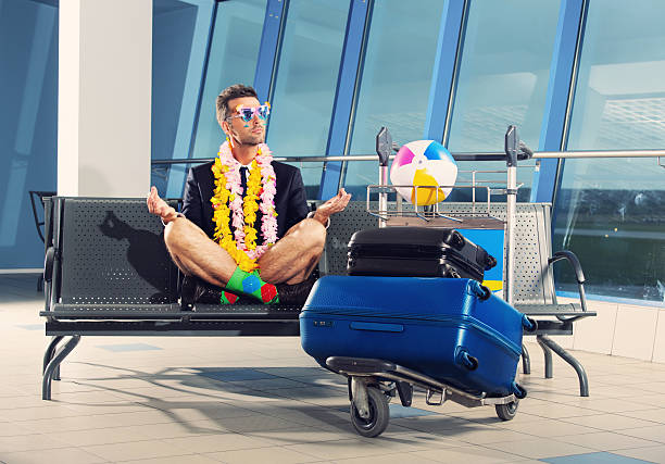 Going on holiday Portrait of businessman in a vacation mood, wearing beach shorts, garlands and sunglasses, sitting in yoga pose and waiting for the flight at the airport. luggage cart stock pictures, royalty-free photos & images
