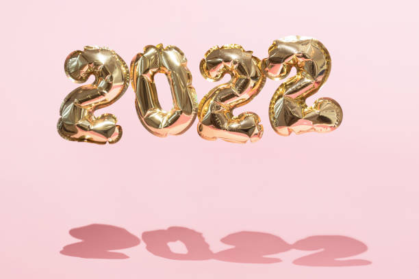 Gold 2022 balloons on a pink background with confetti and Christmas shiny balls, flat lay. New Years celebration concept stock photo