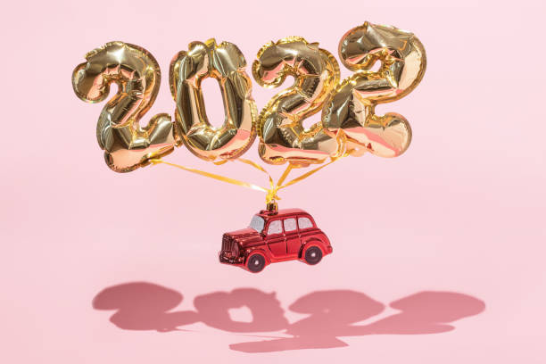 Gold 2022 balloons with red toy car on a pink background with confetti and Christmas shiny balls, flat lay. New Years celebration concept stock photo
