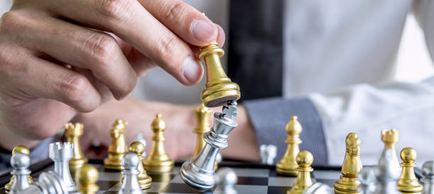 Gold and silver chess with player, Hands of businessman moving chess figure in competition to planning strategy to success play for win stock photo