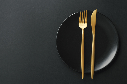 Beautiful gold cutlery - fork and knife on black plate on black background. Top View, above. Horizontal.