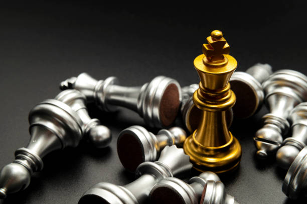 gold queen chess surrounded by a number of fallen silver chess pieces stock photo