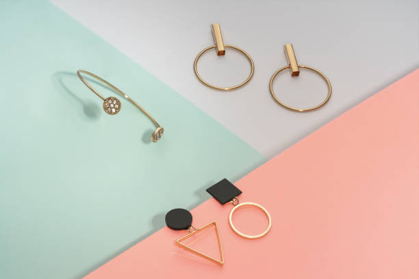 golden bracelet and two golden geometric earrings pairs on pastel colors background pink and blue - joias imagens e fotografias de stock