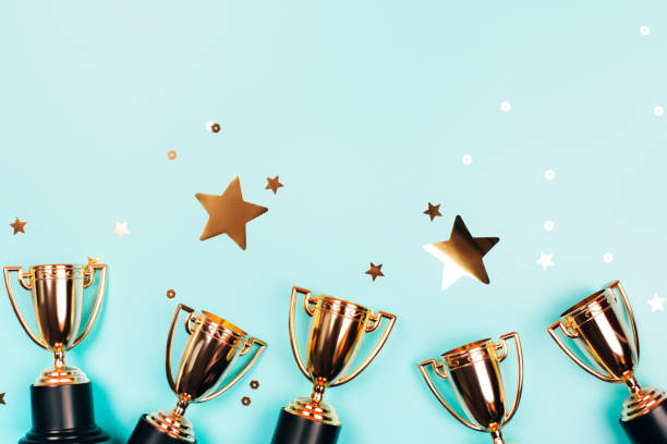 Golden cups of winner Golden cups of winner with shiny confetti on a blue background with copy space. Flat lay style. trophy award stock pictures, royalty-free photos & images