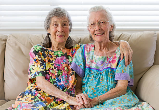 Golden Friends Two elderly widow friends sitting on a couch holding hands. neicebird stock pictures, royalty-free photos & images