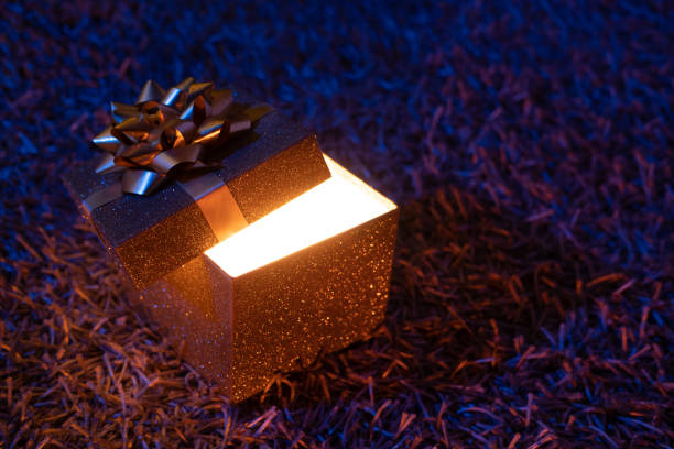 Golden gift box with bright light shining out at night. stock photo