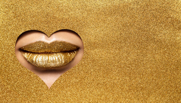 Golden Lips Make up. Gold Beauty Woman Makeup Face. Gold Lipstick Close peek out Glitter Yellow Paper Background. Luxury Make up Cosmetic Salon Treatment stock photo
