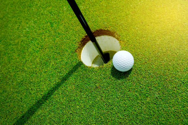 Golf ball almost in the hole on the grass White golf ball near the hole on the green grass close to stock pictures, royalty-free photos & images