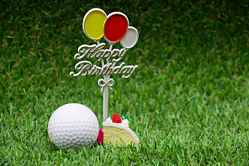Golf ball with Happy birthday sign on green grass.