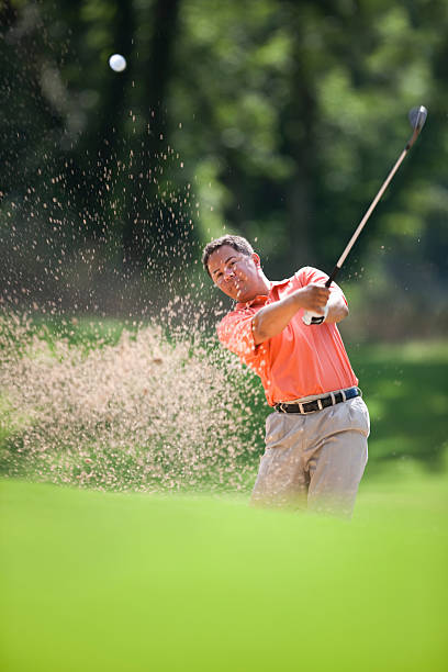 Golfer Hitting Golf Ball In Sand Hazard Action shot of Hispanic man golfing, showing sand & golf ball in mid air. texas shooting stock pictures, royalty-free photos & images