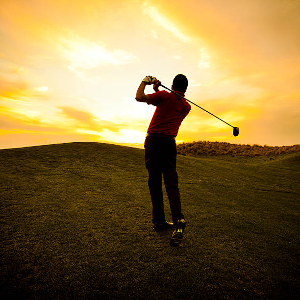 Golfer swinging at sunset stock photo
