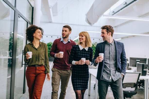 Good friends make an excellent team Group of diverse coworkers walking through a corridor in an office, holding paper cups business casual stock pictures, royalty-free photos & images