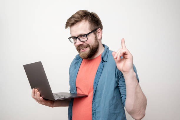 Good idea. Satisfied man holds a laptop in hands, he has a solution to the problem, he raises finger up and looks intriguingly. stock photo