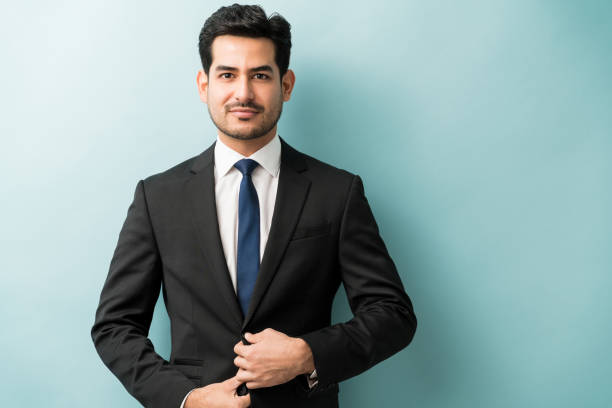Good Looking Male Business Professional In Studio Young male entrepreneur making eye contact against blue background suit stock pictures, royalty-free photos & images