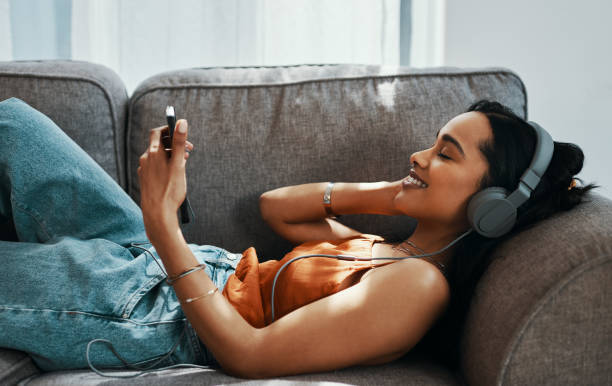Good music finds it's way to your heart Shot of a young woman using a smartphone and headphones on the sofa at home listening stock pictures, royalty-free photos & images