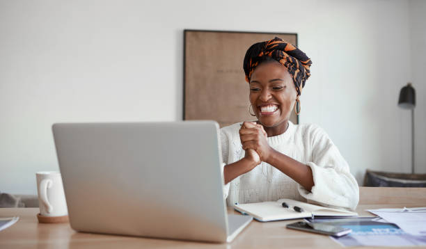 A good opportunity just made its way to her Shot of a young woman cheering while working on a laptop at home employee stock pictures, royalty-free photos & images