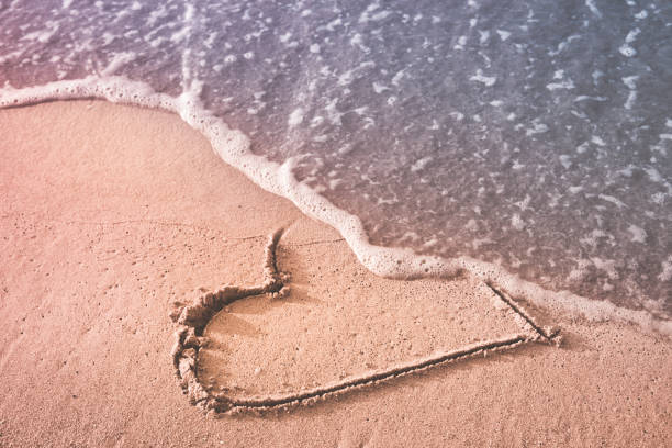 Goodbye love Heart drawn on the beach sand being washed away by a wave. Love affair, summer love or breakup and divorce concept. Ephemeral romantic love. Not true love. End of relationship. divorce beach stock pictures, royalty-free photos & images